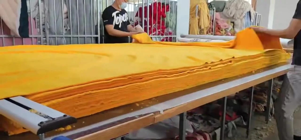 Workers spreading yellow fabric on a factory cutting table